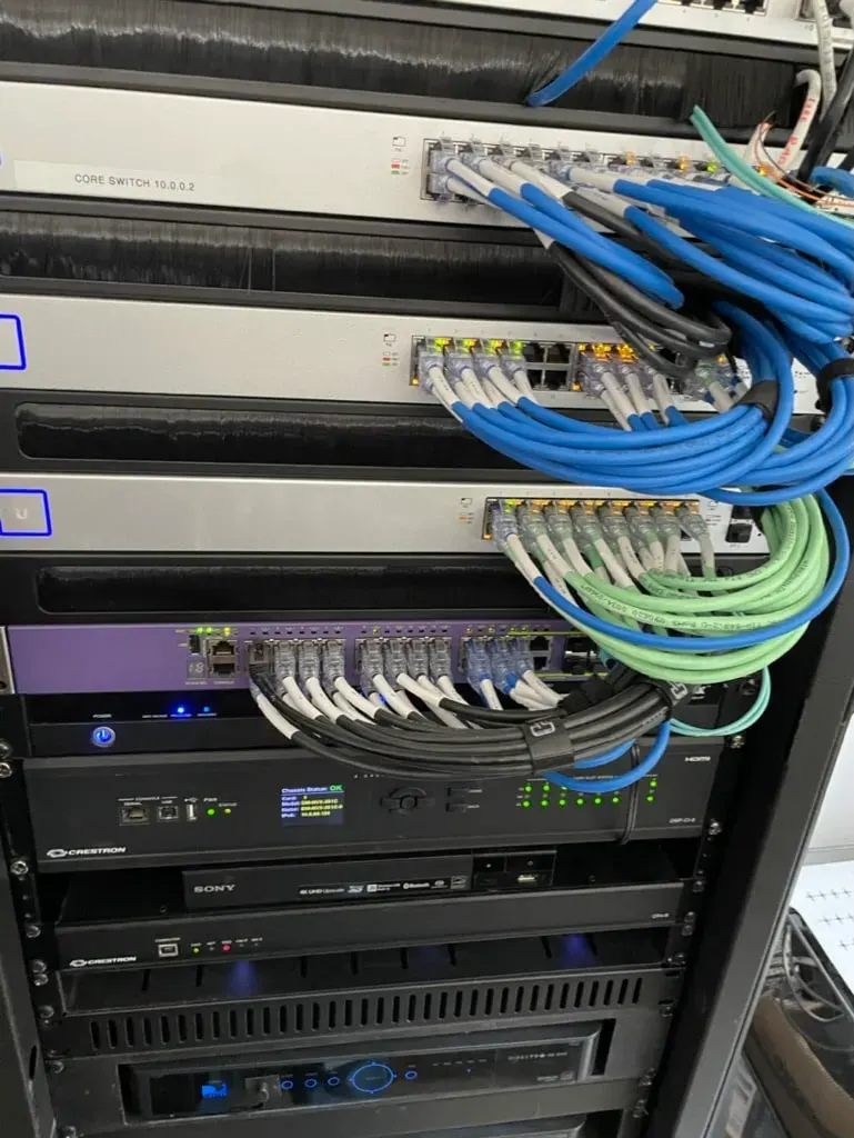 A labeled, color-coded equipment rack — core switch, Crestron processors, structured cabling
